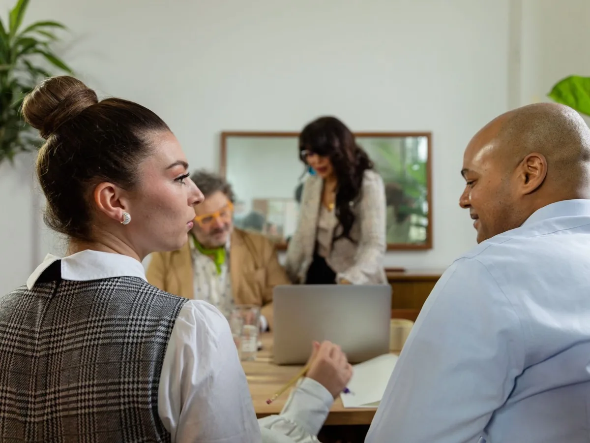 Three people talk around a table in an office.