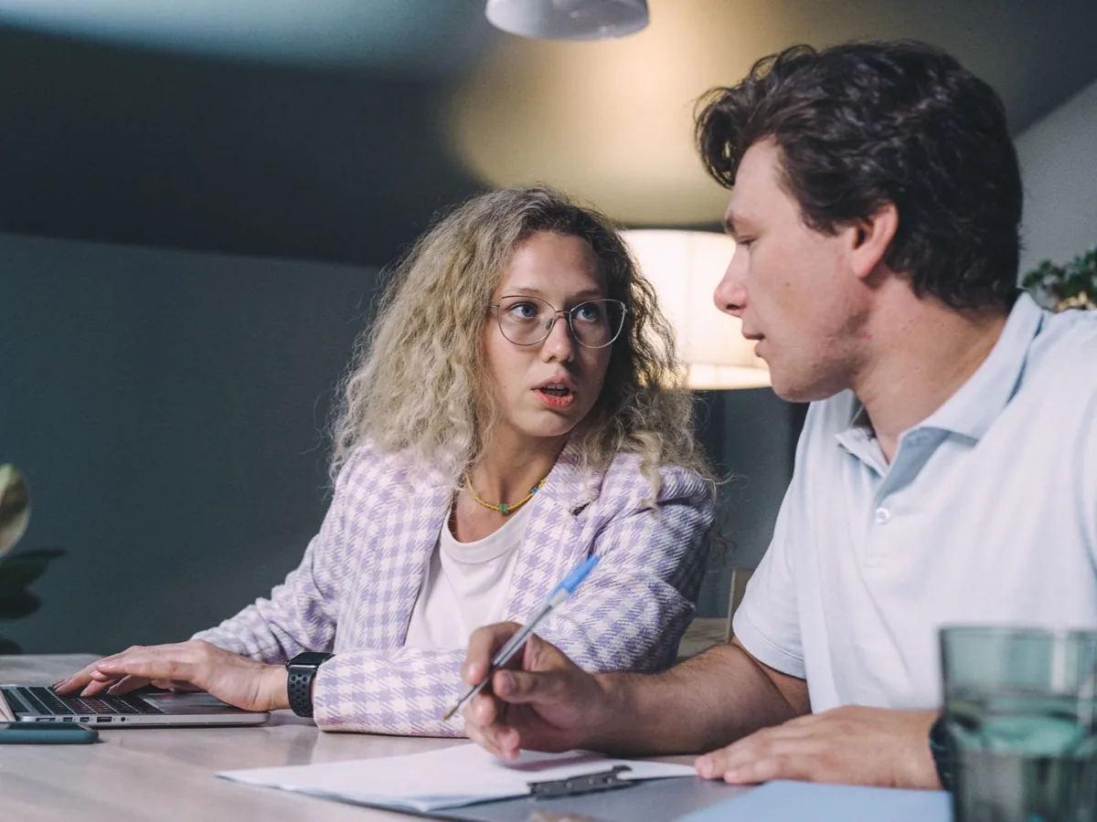 Two colleagues look at a laptop together at a desk.