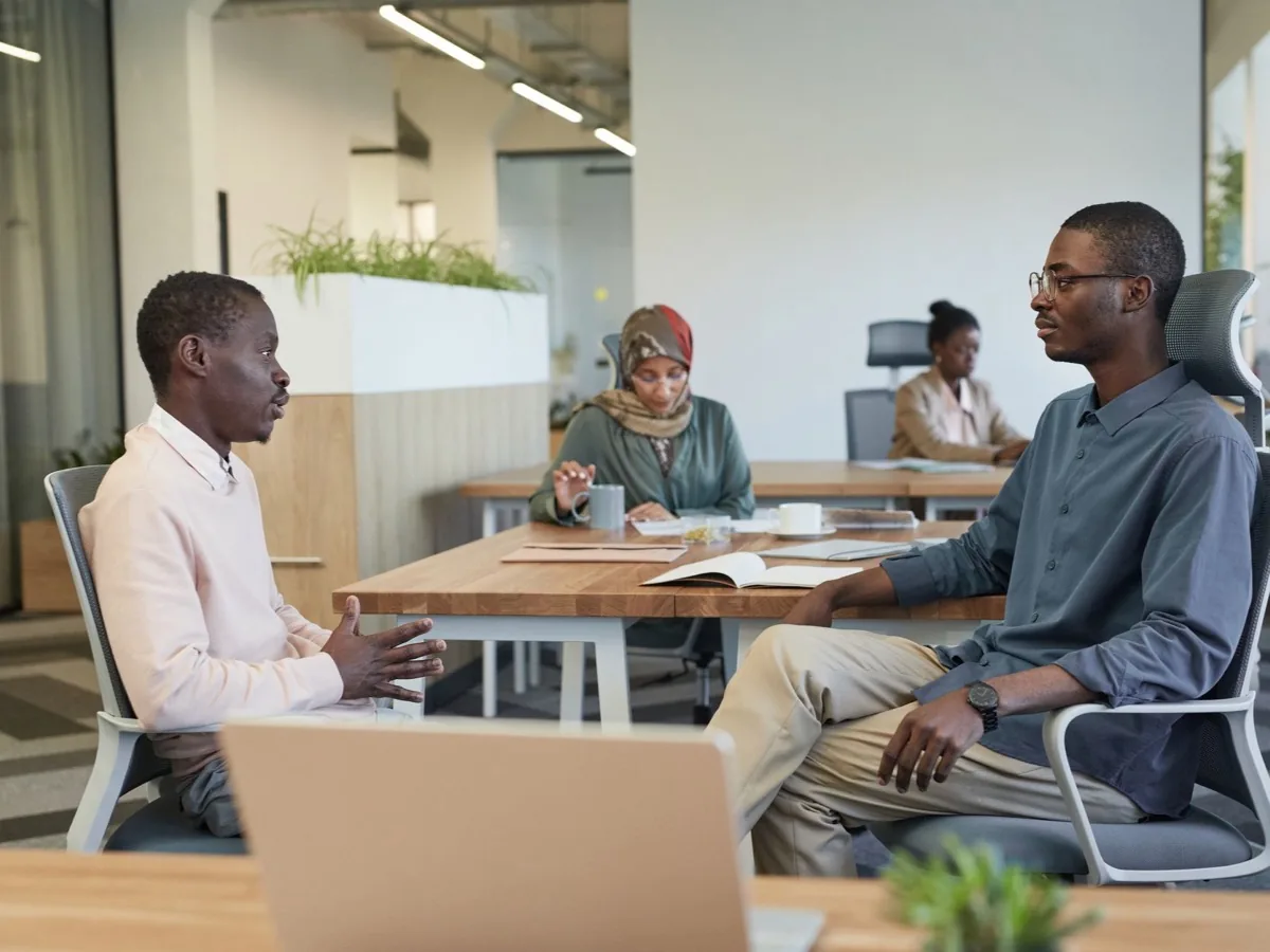 Three colleagues sit at a table in an open plan office.