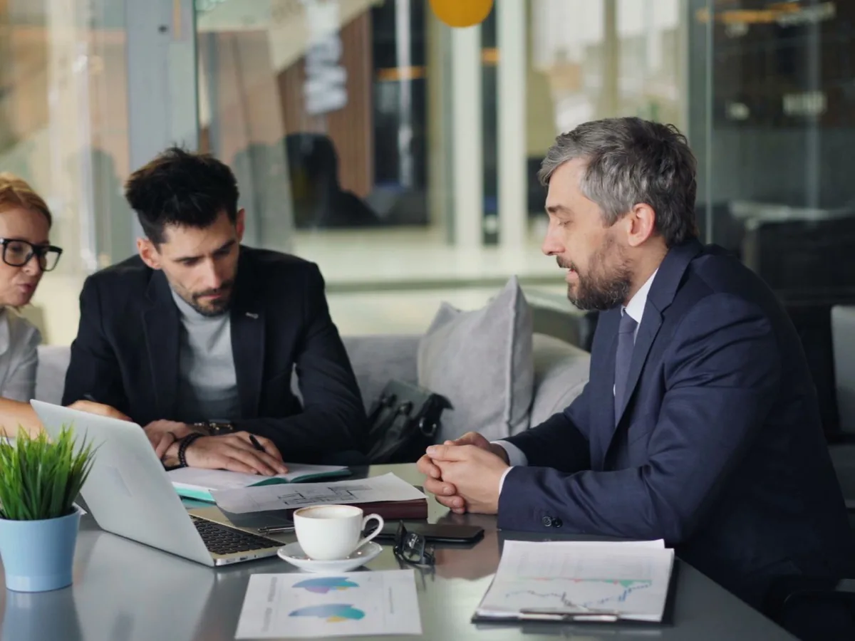 Three people sit around a laptop in a meeting room.